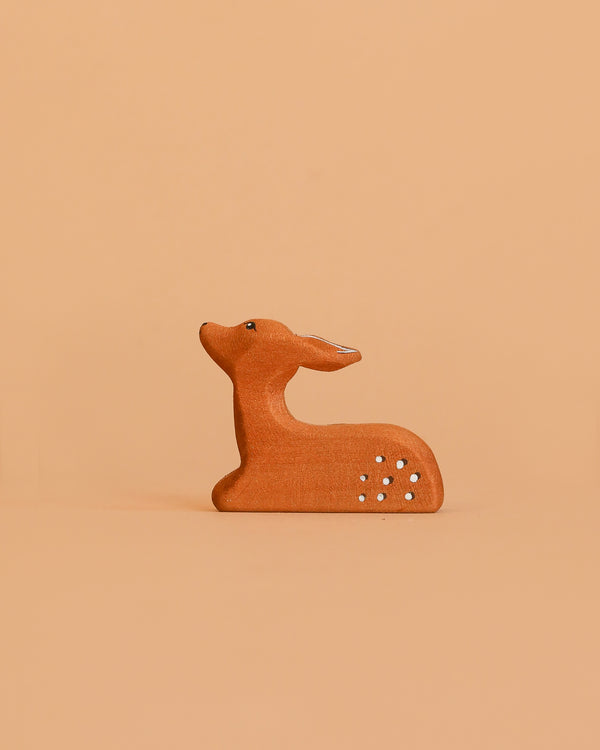 The Bumbu Handmade Wooden Fawn Resting features a small, handcrafted brown design with white spots. Its minimalistic look and eco-friendly wood make it a charming toy or decor piece for any space. The fawn gazes upward as it rests.