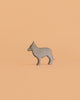 The Bumbu Handmade Wooden Wolf Cub, a small gray handcrafted figurine, stands on a solid peach-colored background.