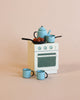 The Maileg Kitchen Set with Grandma & Grandpa features a small white toy stove, blue cookware, two cups, a teapot, and pans with food—evoking the charming world of Maileg mice. Presented against a pale beige background, this set pairs perfectly with a Maileg kitchen or the classic Maileg metal fridge for delightful pretend play.