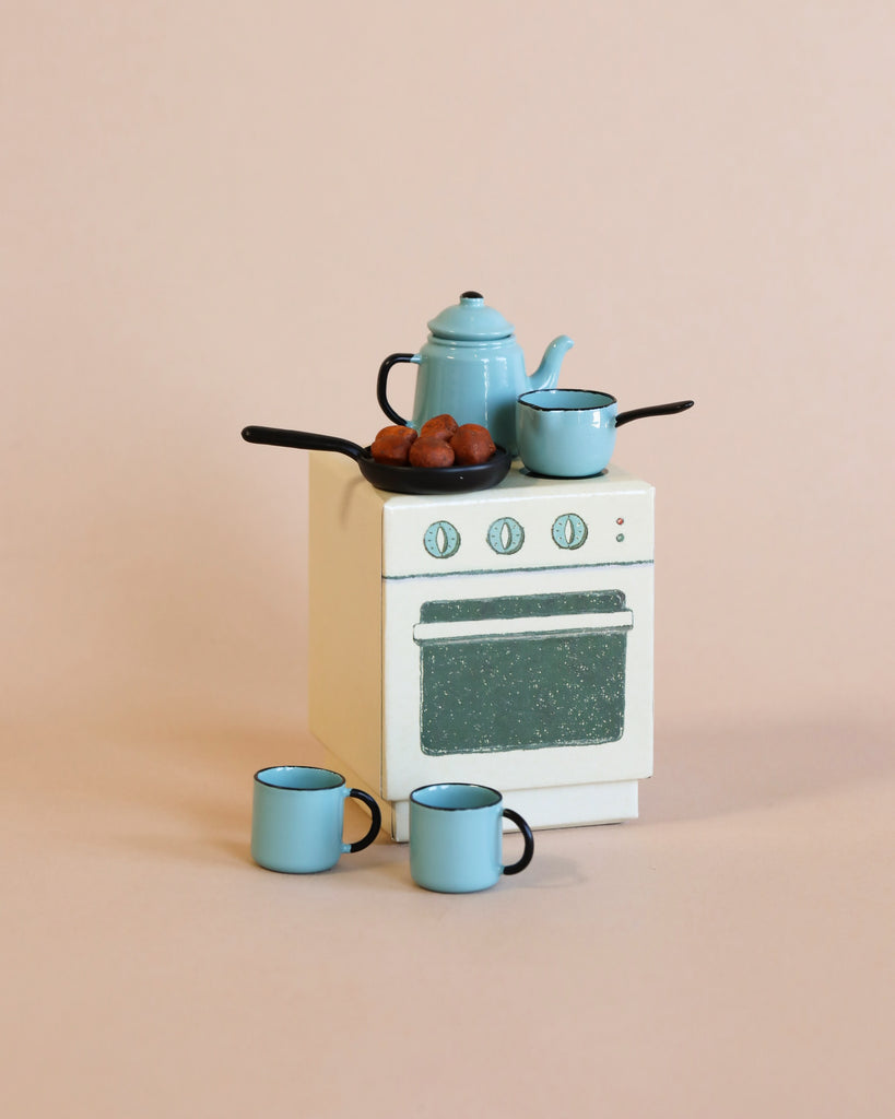 A miniature Maileg Suitcasa Furnished Set stove featuring a teapot, a small pan of meatballs, a saucepan on top, and two mugs in front.