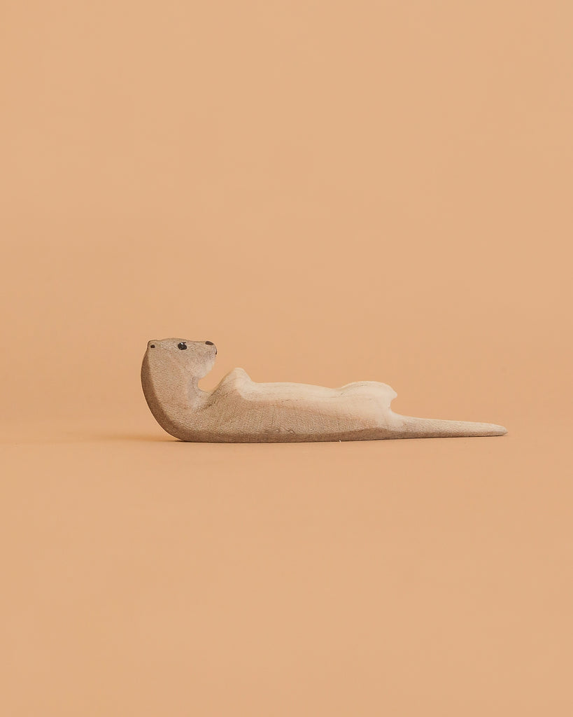 The Bumbu Handmade Wooden Otter Set features small, minimalist otters lying on their backs—eco-friendly toys ideal for thoughtful decor or imaginative play, shown against a peach-colored background.