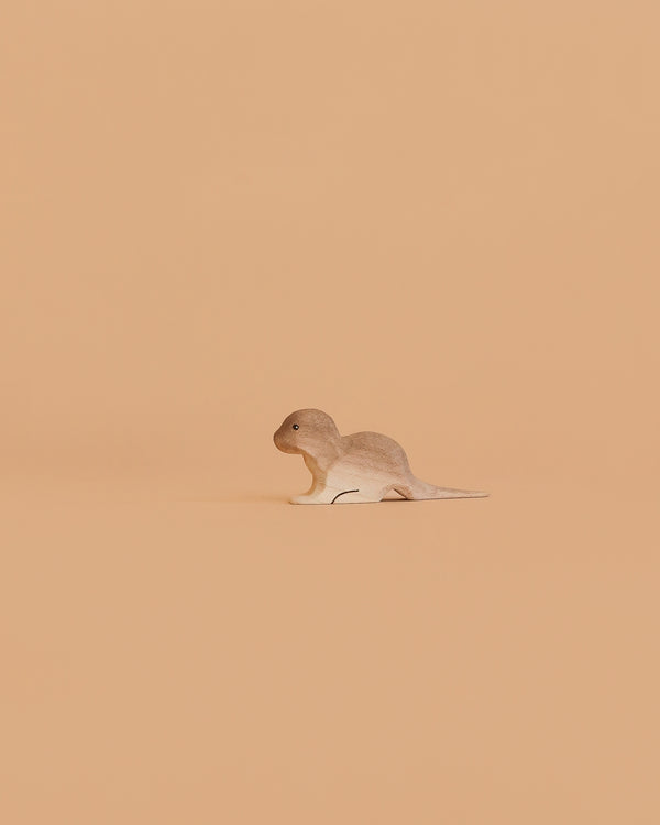The Bumbu Handmade Wooden Baby Otter toy stands slightly left on a plain, peach-colored background.