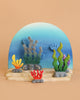 A colorful wooden diorama features blue, green, yellow, and red seaweed and coral on a blue and tan background—perfect to pair with the Bumbu Handmade Wooden Ocean Set.