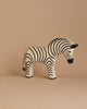 A handcrafted zebra figurine from the Ostheimer Handmade Wooden Safari Animals Set stands on a beige surface against a matching background, perfect for imaginative play and reminiscent of classic wooden toys.