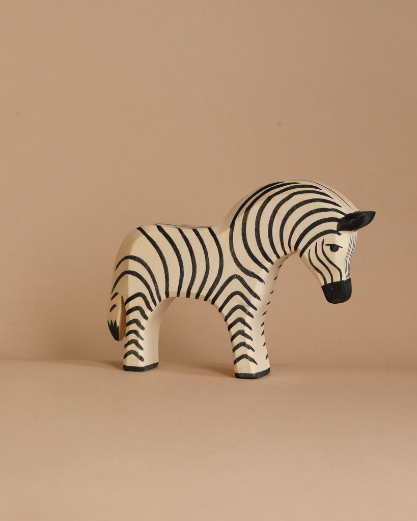 A handcrafted zebra figurine from the Ostheimer Handmade Wooden Safari Animals Set stands on a beige surface against a matching background, perfect for imaginative play and reminiscent of classic wooden toys.