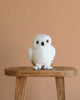 The Steiff Harry Potter "Hedwig" Owl 8" plush, featuring yellow eyes, sits on a wooden stool against a beige background—an ideal gift for any Harry Potter fan.