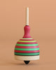 The Mader Fridolin Spinning Top - Green and Red features bold stripes and stands upright on a smooth surface against a plain peach background.