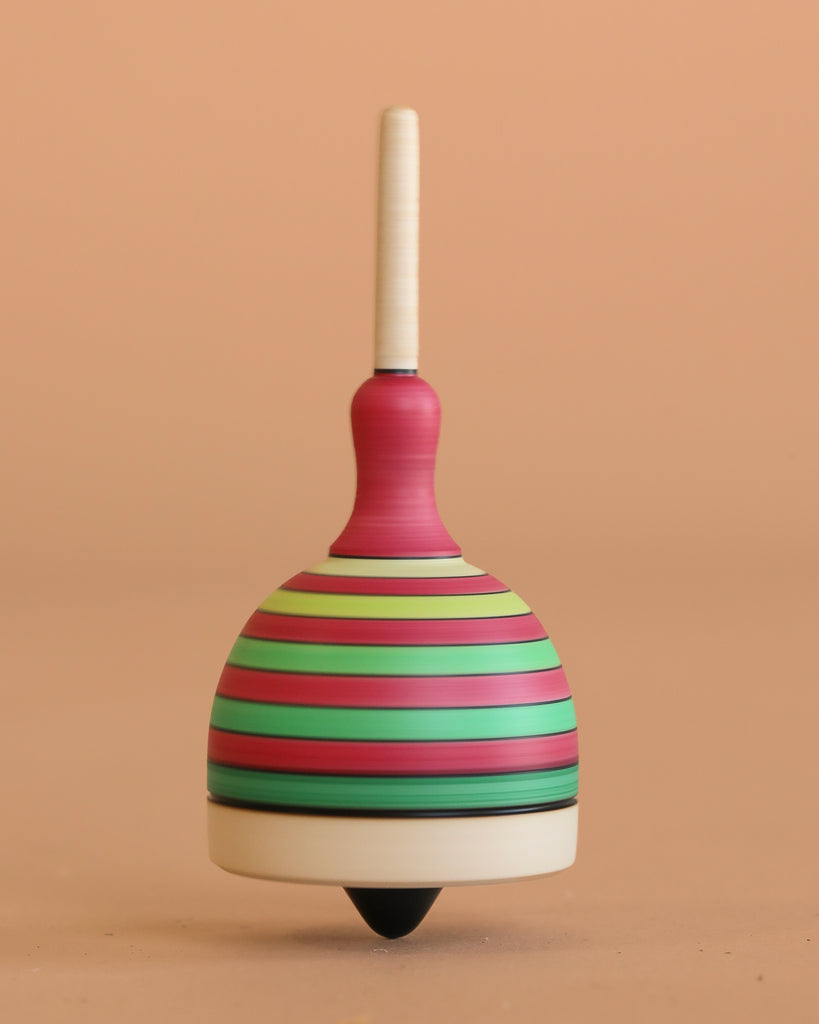 The Mader Fridolin Spinning Top - Green and Red features bold stripes and stands upright on a smooth surface against a plain peach background.