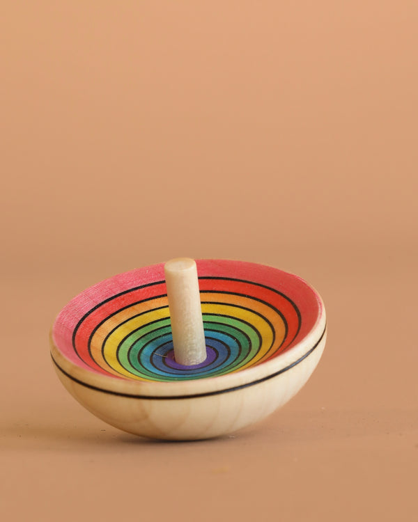 The Mader UFO Spinning Top - Red Rainbow features vibrant rainbow rings on maple wood, displayed against a plain beige background.