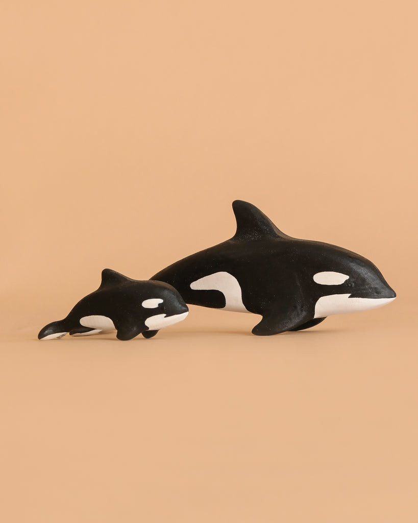 The Bumbu Handmade Wooden Orca Set features two black and white orca figurines, one large and one small, placed side by side on a beige background—ideal for Montessori-inspired imaginative play.