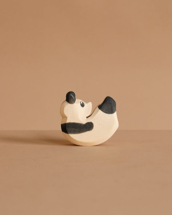 The Ostheimer Panda Bear, Small is a handcrafted wooden figurine with simple black and white details, shown lying on its back against a light brown surface and matching background. Inspired by classic Ostheimer toy design.