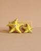 The Bumbu Handmade Wooden Yellow Starfish Set features two upright yellow wooden starfish with blue dots—one large, both with five arms—displayed against a beige block, making them ideal Montessori toys for creative, hands-on learning.