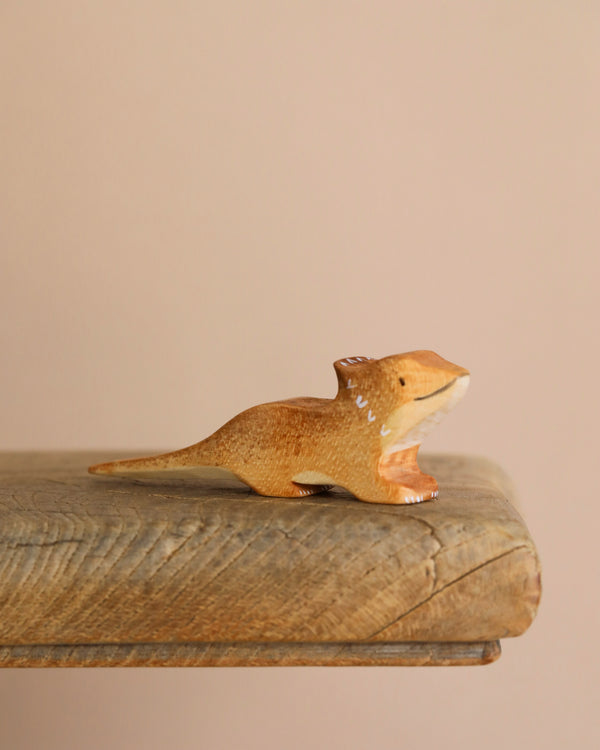 The Bearded Dragon Wooden Animal is a small, brown dinosaur figurine crafted from sustainable hardwood. It features a long tail and short legs, resting on a wooden surface against a neutral backdrop. Its glossy finish with white accents enhances its charm, resembling an intricately crafted lizard toy.