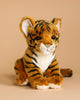The Safari Tiger Family Set features plush toy tigers with orange and black stripes, white paws, and a white muzzle sitting on a neutral beige surface against a matching background.