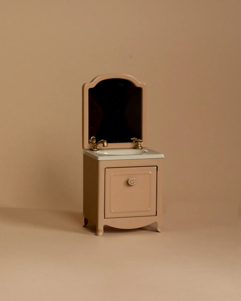 A small beige Maileg Bathroom Set with a mirror and gold faucet, featuring a single-door vanity design against a plain beige background—ideal for creating a minimalist look in Maileg mouse furniture displays.