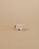 A small, light-colored animal figurine from the Ostheimer Handmade Wooden Farm Animals Set stands on a beige surface with a matching background; this handcrafted toy features a short tail and subtle red accents on its face.