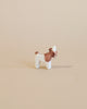 A small donkey from the Ostheimer Handmade Wooden Farm Animals Set, painted white and brown with non-toxic paints, stands on a plain beige background.