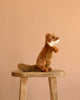 A Weasel Stuffed Animal with realistic features sits upright on a wooden stool against a plain beige background.