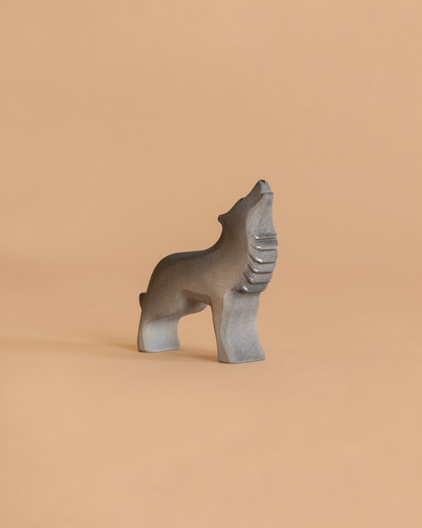 The Bumbu Handmade Wooden Wolf Howling sculpture, in a minimalist gray design, stands on a smooth light brown surface with a matching plain background.