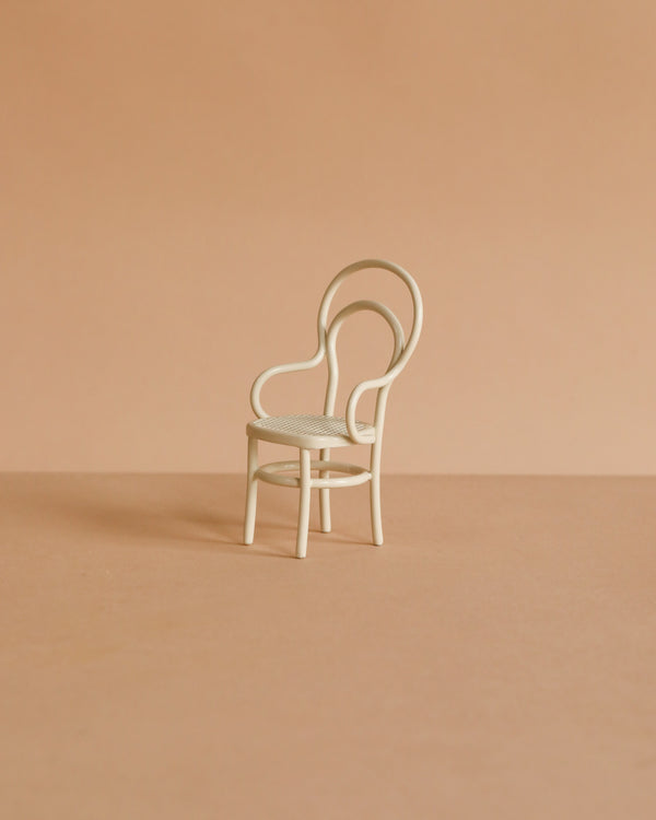 The Maileg Vintage Chair, Mouse Size - Off White is a small, white metal chair with a rounded backrest, ideal for mouse-sized furniture collections. Shown on a light brown surface with a beige background.