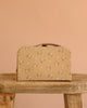 The Maileg Little House Bathroom Set, featuring charming mouse-sized pieces with a beige and floral design and brown accents, rests on a rustic wooden table against a peach-colored background.