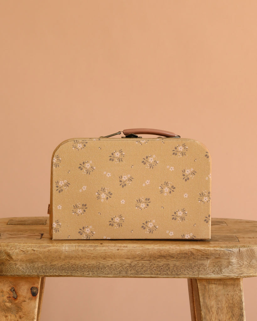 The Maileg Little House Bathroom Set, featuring charming mouse-sized pieces with a beige and floral design and brown accents, rests on a rustic wooden table against a peach-colored background.