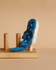 The Finger Puppet: Whale Shark, a blue and white felt plush with white spots, sits upright on a wooden rack with two vertical pegs against a plain beige background.
