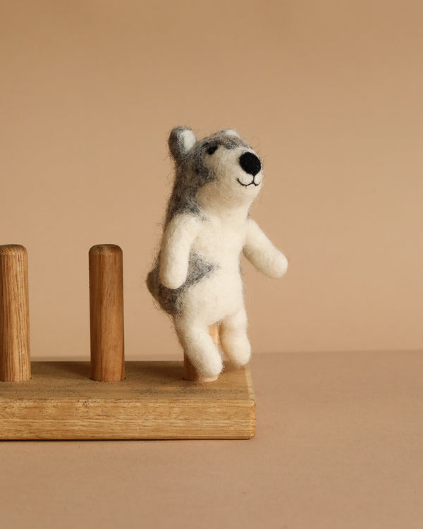 The Felt Finger Puppet: Alaskan Husky Dog, a small handmade item crafted from soft wool felt, stands upright on a wooden stand against a neutral beige background.