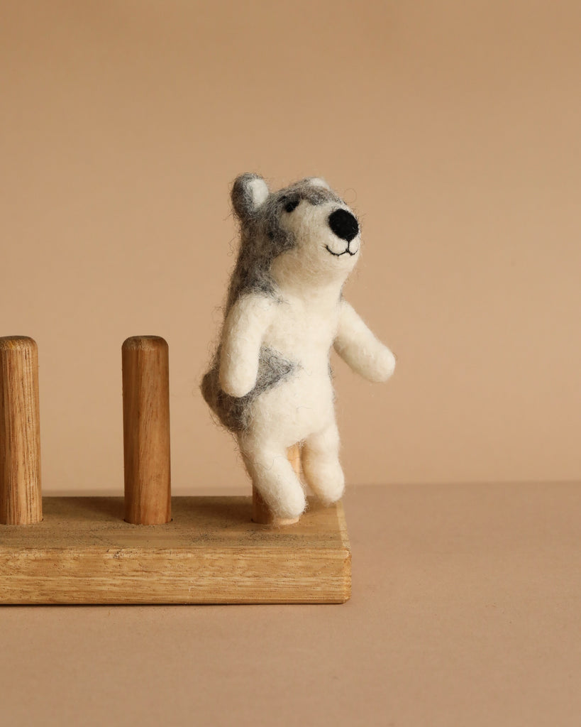 The Felt Finger Puppet: Alaskan Husky Dog, a small handmade item crafted from soft wool felt, stands upright on a wooden stand against a neutral beige background.