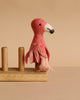 The Flamingo Finger Puppet, handmade with pink and light pink felted details, sits on a wooden stand against a beige background, inspiring imaginative play.