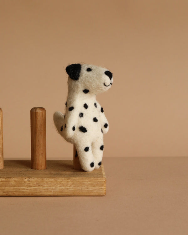 The Felt Finger Puppet: Dalmatian is a small, felted dog with black spots sitting upright on a wooden stand against a beige background—ideal for imaginative play or as a charming decorative piece.