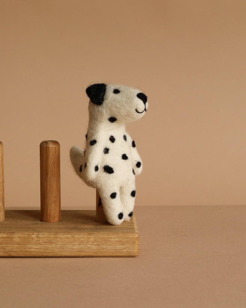 The Felt Finger Puppet: Dalmatian is a small, felted dog with black spots sitting upright on a wooden stand against a beige background—ideal for imaginative play or as a charming decorative piece.