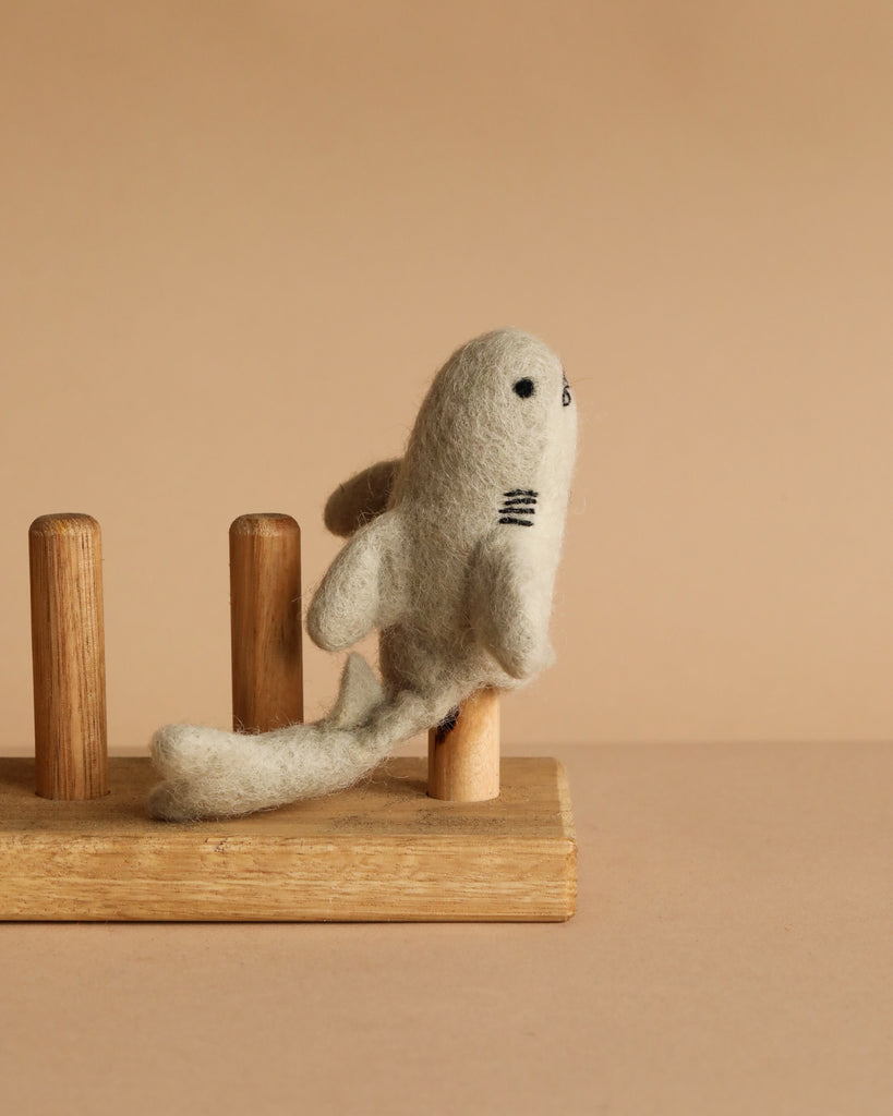The Finger Puppet: Shark is a small, felted puppet with stitched features that stands upright on a wooden peg stand against a beige background—great for imaginative underwater play.