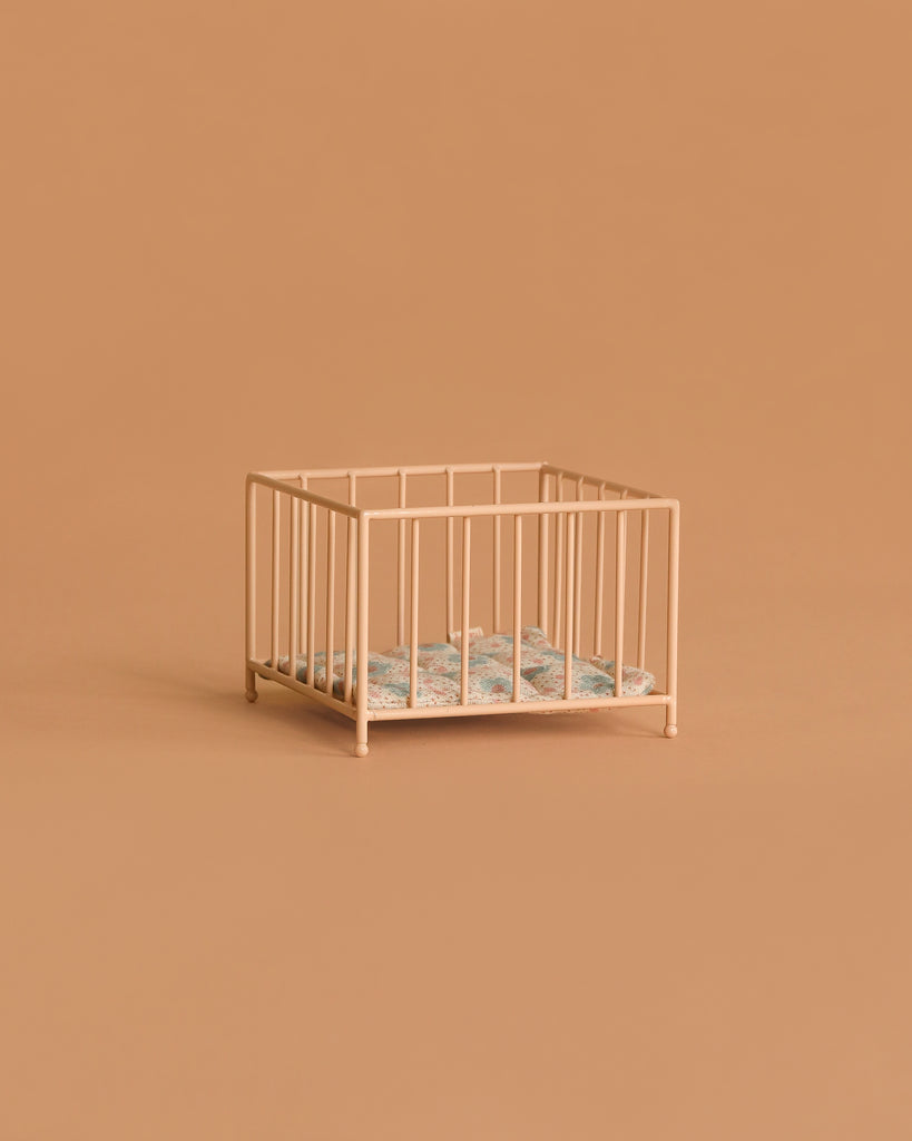 A small, empty Maileg Playpen, My - Rose sits against a beige background, featuring a patterned blanket inside.