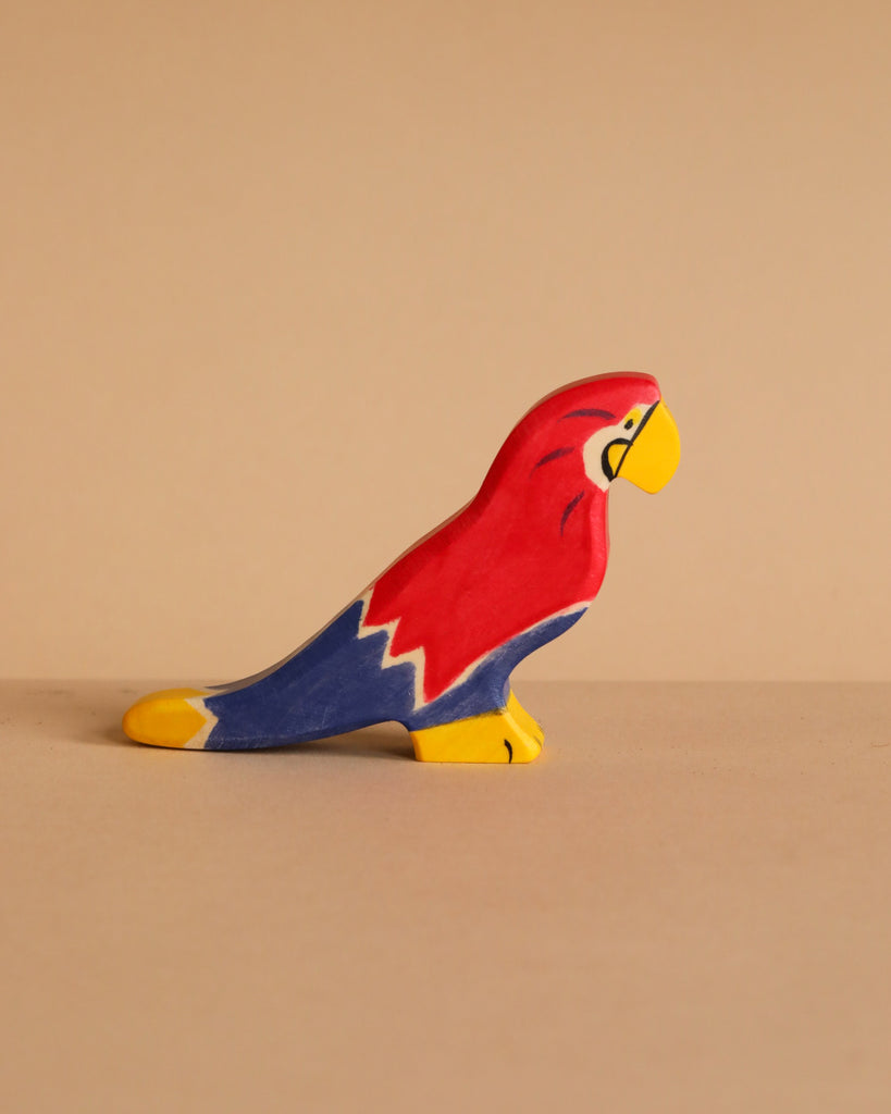 A red, blue, and yellow handcrafted wooden parrot toy from the Holztiger Handmade Wooden Birds of the World Set.