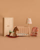 The Maileg Nursery Set includes a white wardrobe, wooden rocking horse mouse, crib with bedding, floral lamp, and pink floral-patterned baby rocker—adorable accessories for your baby mouse.