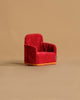 The Maileg Soft Chair - Red, featuring gold trim and a lush texture, rests against a plain beige background. Perfect for Mouse hole Farmhouse settings, it resembles a miniature armchair welcoming your Maileg friends with its vibrant color.