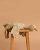 The Senger Naturwelt Cuddly Animal - Linen Goose, made with soft GOTS-certified cotton, rests on a wooden stool against a plain light brown background.