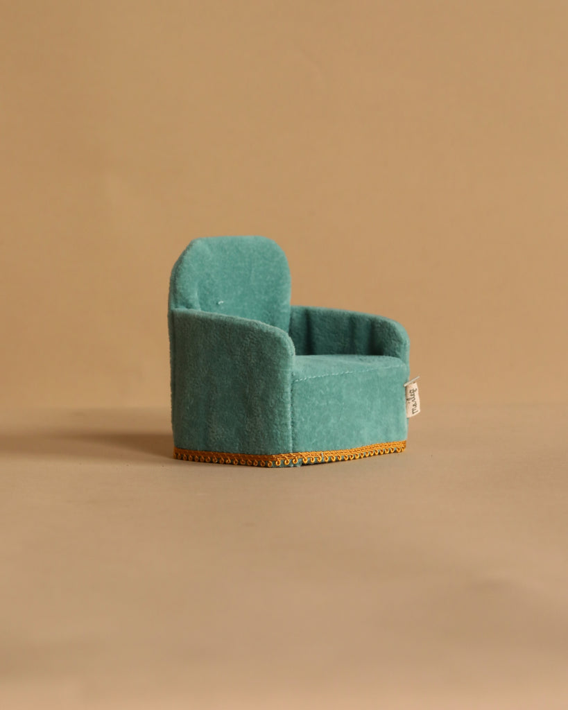 A compact teal velvet suitcase with gold trim rests on a plain beige background. Designed for Maileg On The Go Suitcase Set, it features a rounded top, sturdy handle, and a small white tag attached to the side.