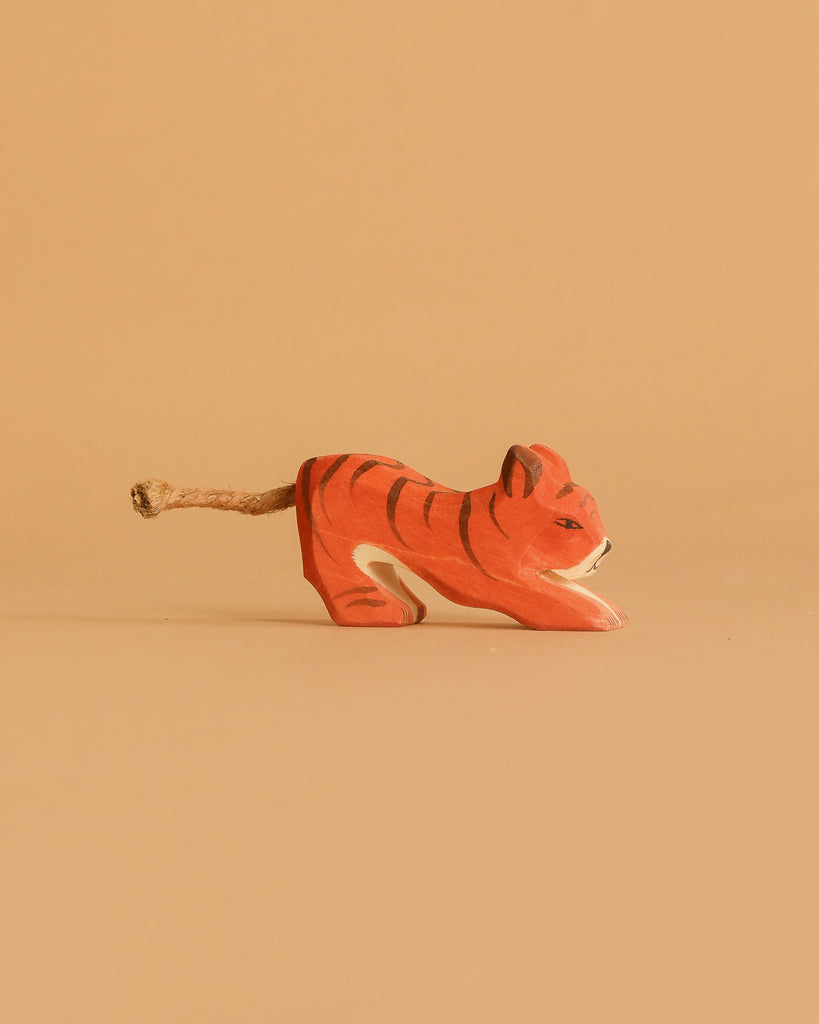 The Ostheimer Tiger Lurking, Small is a handcrafted wooden figurine with orange and black stripes and a rope tail, shown on a plain beige background.