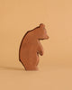 The Ostheimer Large Bear - Standing Head Low is a handcrafted wooden figurine standing on a beige surface, its head lowered and casting a gentle shadow—ideal for imaginative play or to complement your Ostheimer toy collection.