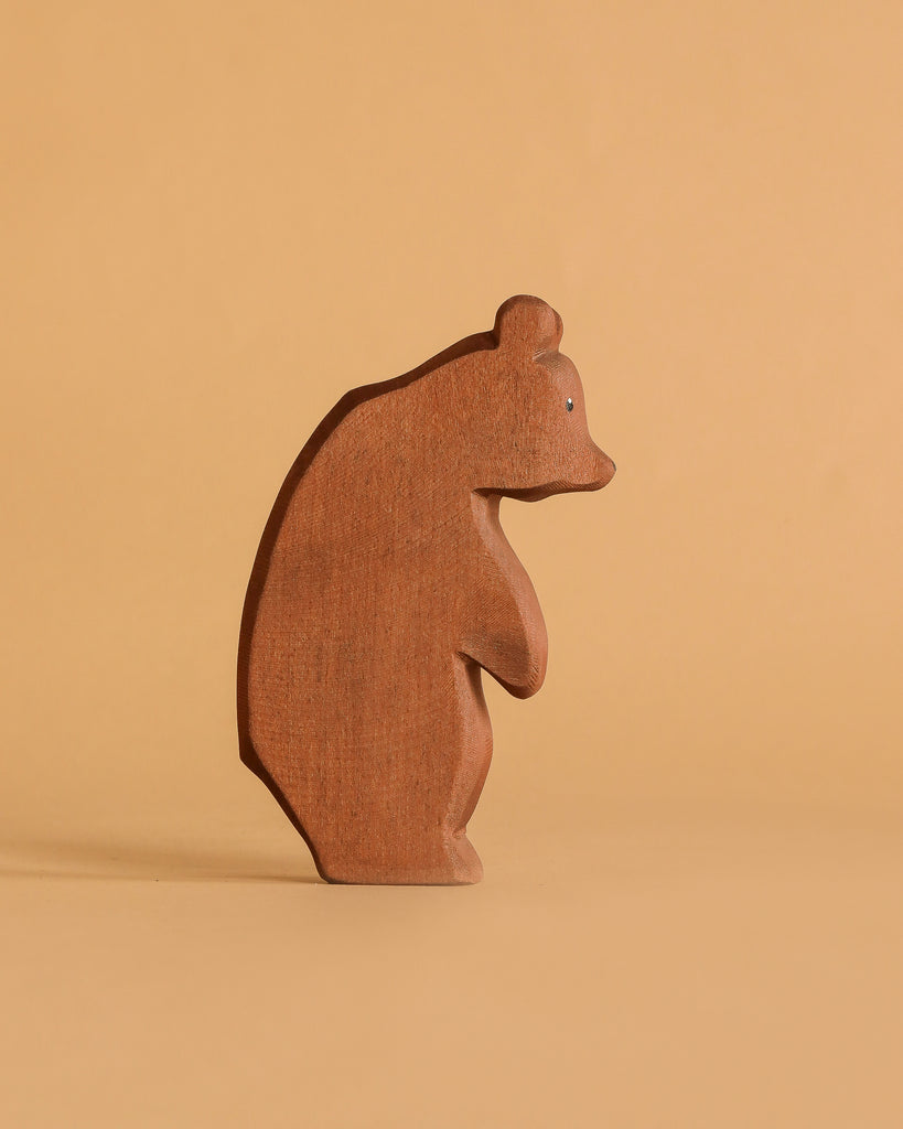 The Ostheimer Large Bear - Standing Head Low is a handcrafted wooden figurine standing on a beige surface, its head lowered and casting a gentle shadow—ideal for imaginative play or to complement your Ostheimer toy collection.