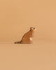 A handcrafted raccoon figurine from the Ostheimer Handmade Wooden Woodland Set sits on a light brown surface with a beige background, featuring hand-painted face and tail details and facing right.
