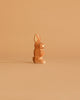 An upright rabbit figurine from the Ostheimer Handmade Wooden Woodland Set is shown on a plain light brown background. The simple carving features upright ears and minimal facial details for a cute, minimalist look.