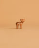A small brown wooden deer from the Ostheimer Handmade Wooden Woodland Set stands on a matching light brown background, reflecting the charm and tradition of Ostheimer’s sustainably crafted toys.