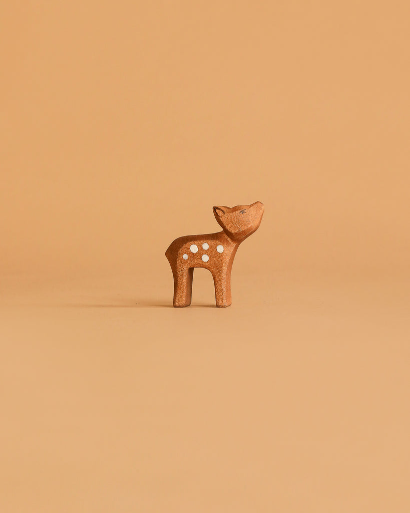 A small brown wooden deer from the Ostheimer Handmade Wooden Woodland Set stands on a matching light brown background, reflecting the charm and tradition of Ostheimer’s sustainably crafted toys.