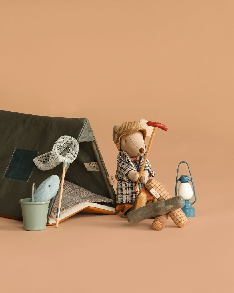 The Maileg Camping Set with Granddad features a toy mouse in a plaid coat by a cozy tent, holding a red-handled tool. Classic accessories—like a butterfly net, bucket with toy fish, blue lantern, and campfire—complete the beige background scene.