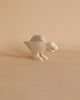 A small, light-colored Handmade Tiny Wooden Spinosaurus Dinosaur stands on a neutral, pale background. The dinosaur has a simple, minimalist design with a rounded body, four legs, a large tail, and minimal facial features. This unique handcrafted decoration pairs beautifully with hand-carved wooden animals for an eco-friendly touch.