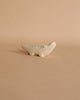 The Handmade Tiny Wooden Safari Animals - Alligator is a small, white ceramic figurine with minimal black detailing on its back and eyes. Set against a plain beige background, the alligator boasts a round snout and a friendly demeanor reminiscent of handcrafted wooden animals.