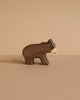 The Holztiger Small Brown Bear, a handcrafted wooden figurine, stands on a light brown surface against a matching beige background.
